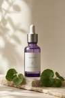 Rooted Calm Serum in a violet-glass dropper bottle among fresh green leaves